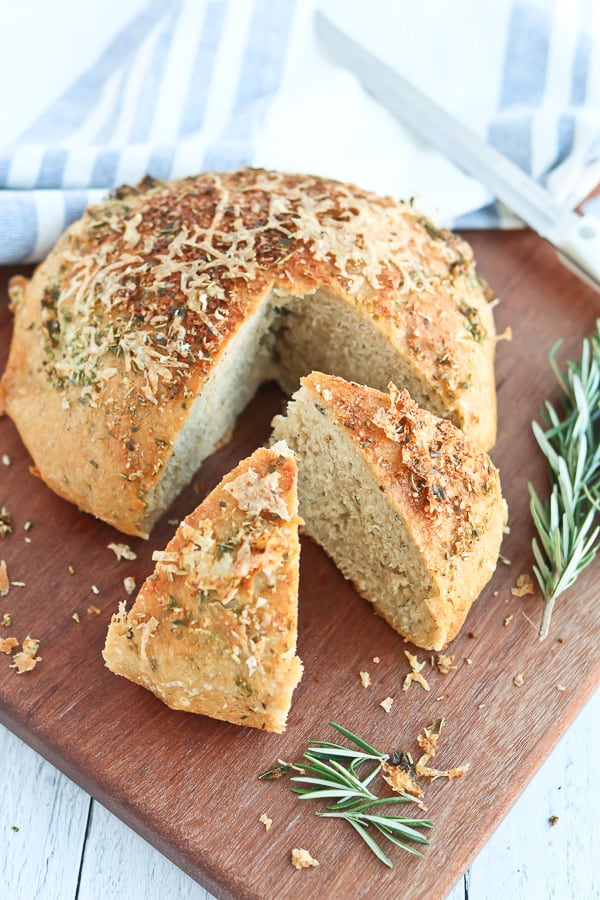 Photo of a round loaf of rosemary bread, with two slices cut.