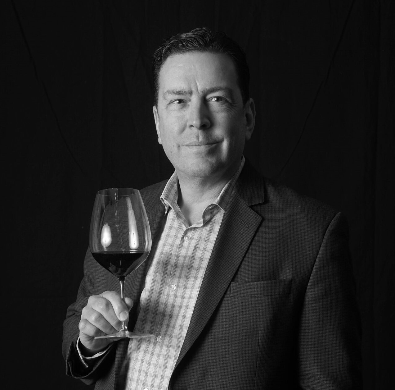 A black and white photo of Lars Leicht holding a glass of wine.