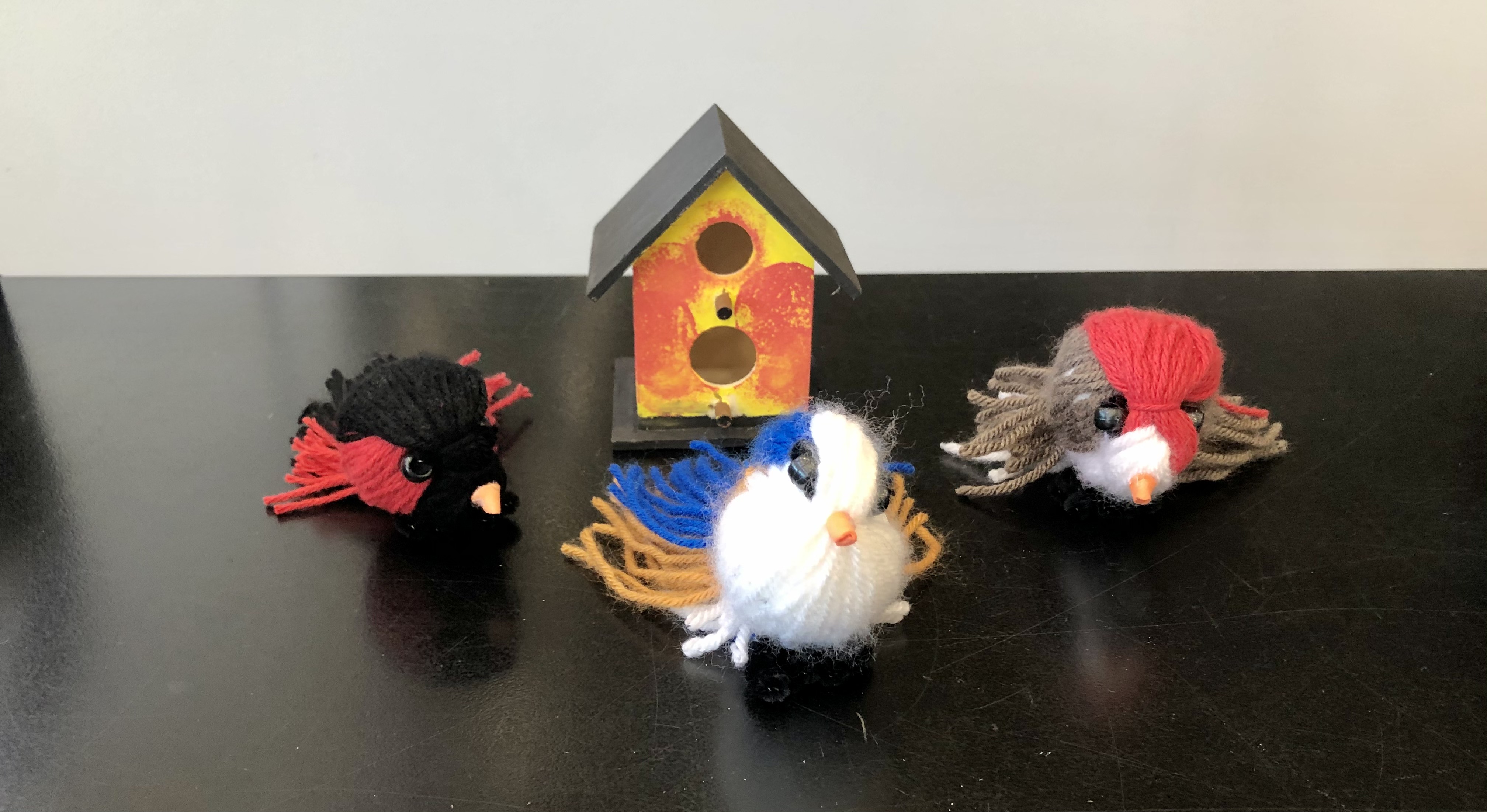 A photo of yarn birds and a min birdhouse.