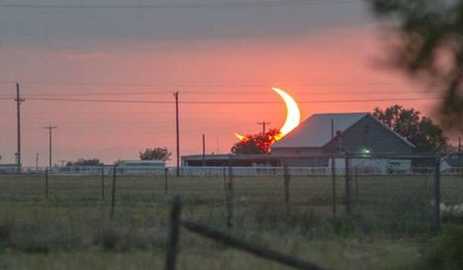 Photo of a partial solar eclipse at sunrise, which creates a scimitar shape on the sun, which is low in the sky.