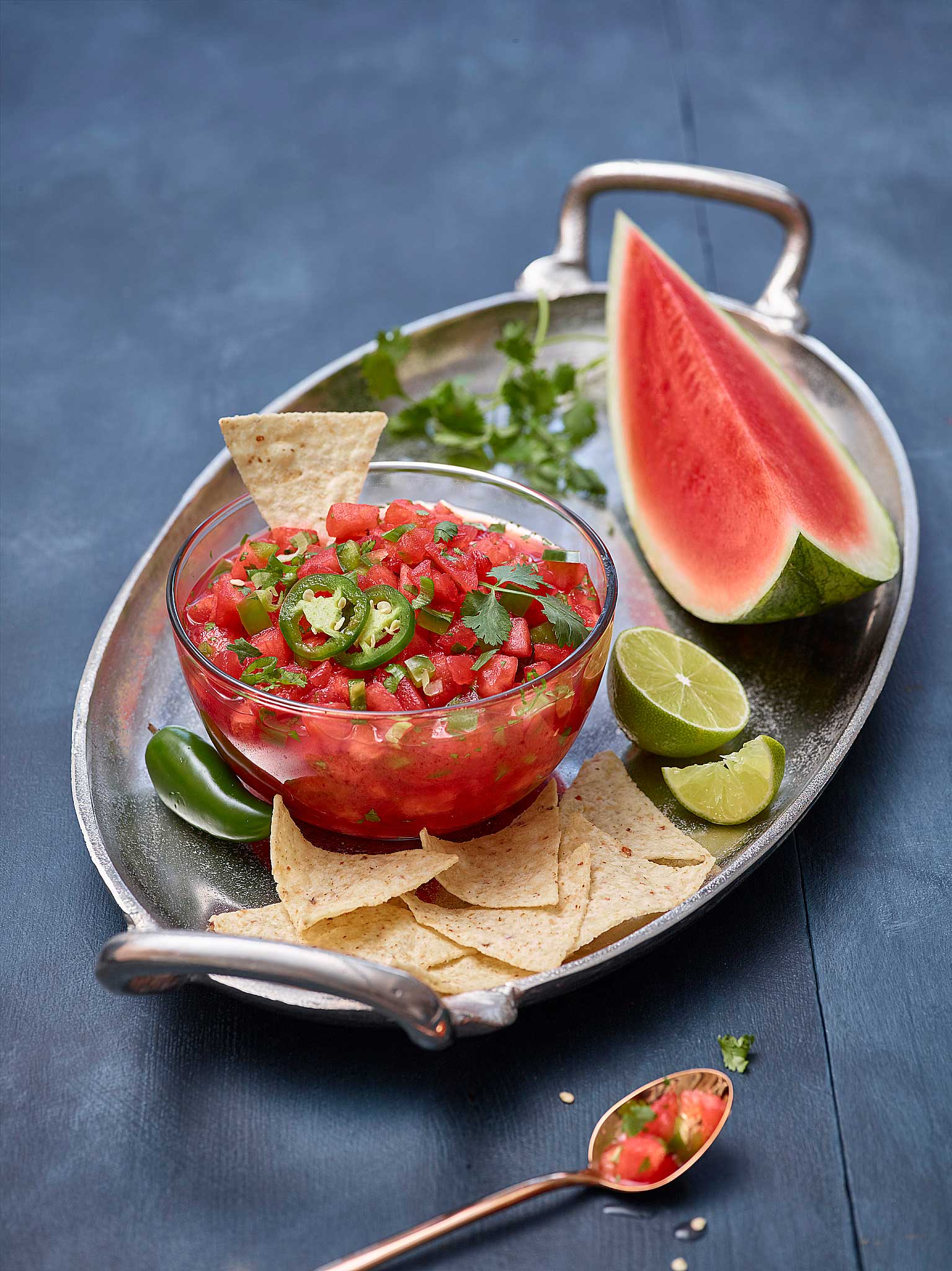Photo of a plate containing a  wedge of watermelon, half a lime, a bowl of watermelon salsa and tortilla chips.