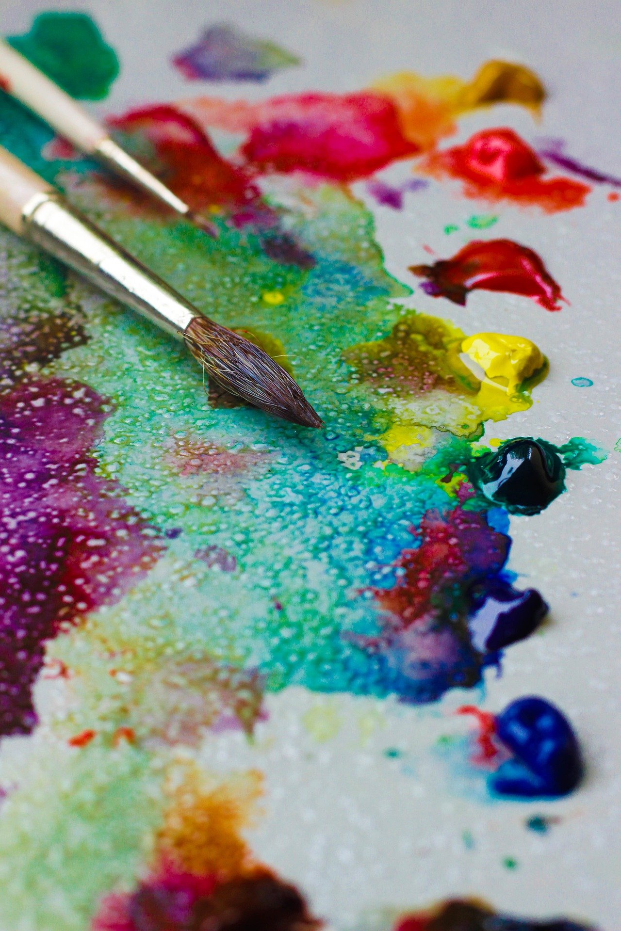 A photo of paintbrushes lying on paper that is dotted with watercolor paint.
