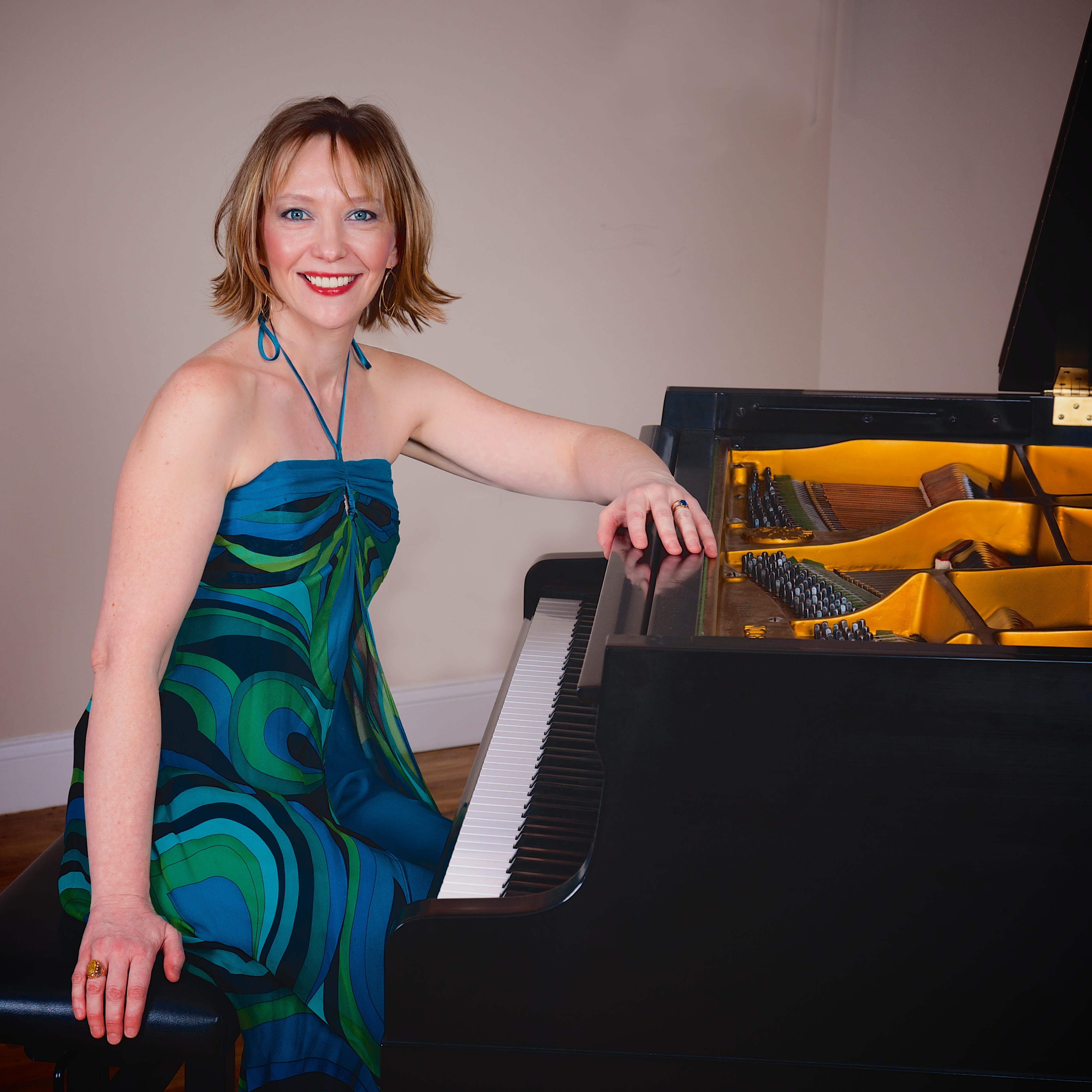 A photo of Oxana Mikhailoff, wearing a blue and green dress, seated at the piano.