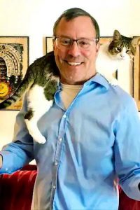 A photo of cat behaviorist Stephen Quandt who has a cat on his shoulder.