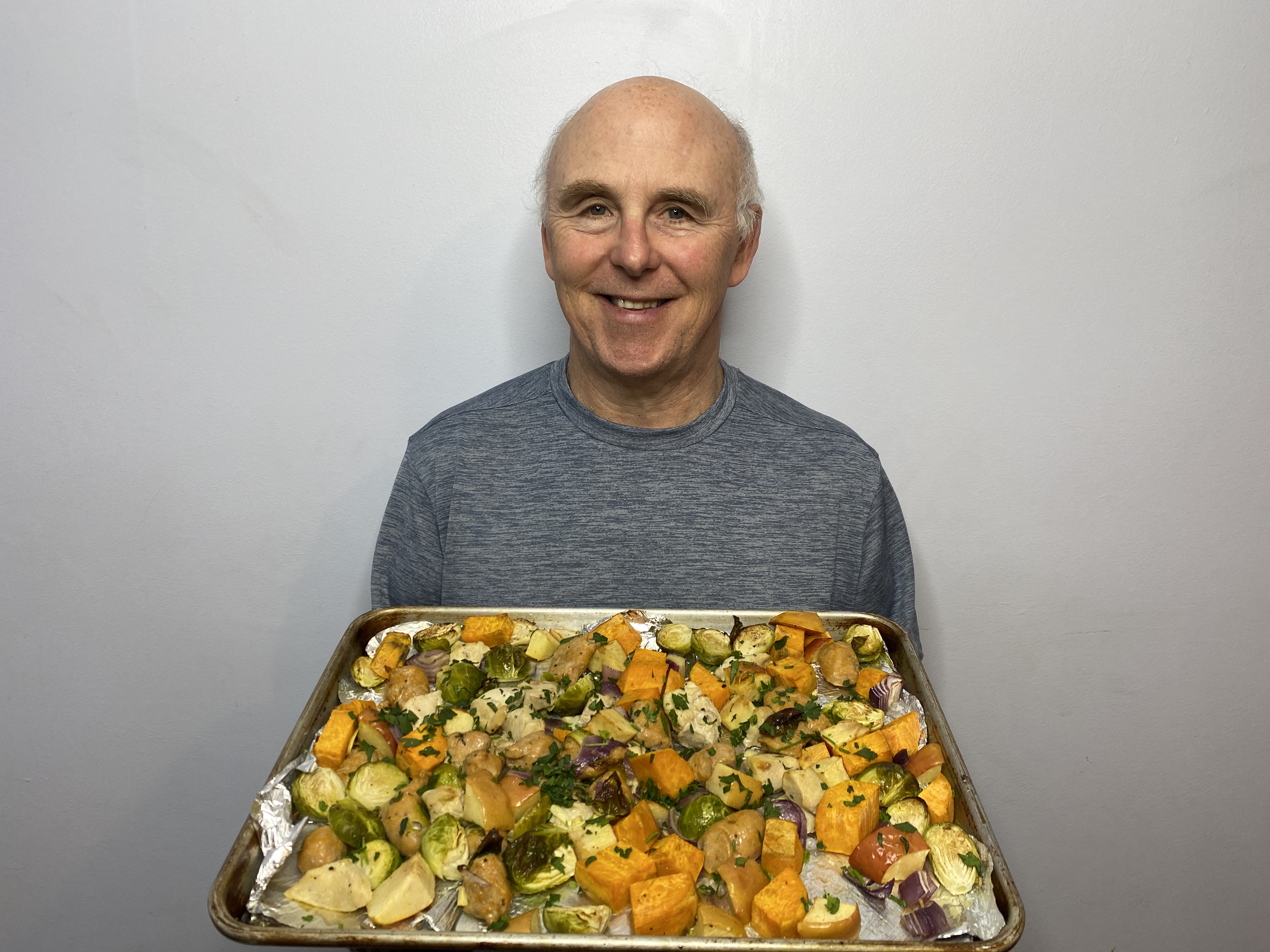 A photo of Chef Rob holding a plate of Autumn Chicken and Sausage Sheet Pan Dinner.
