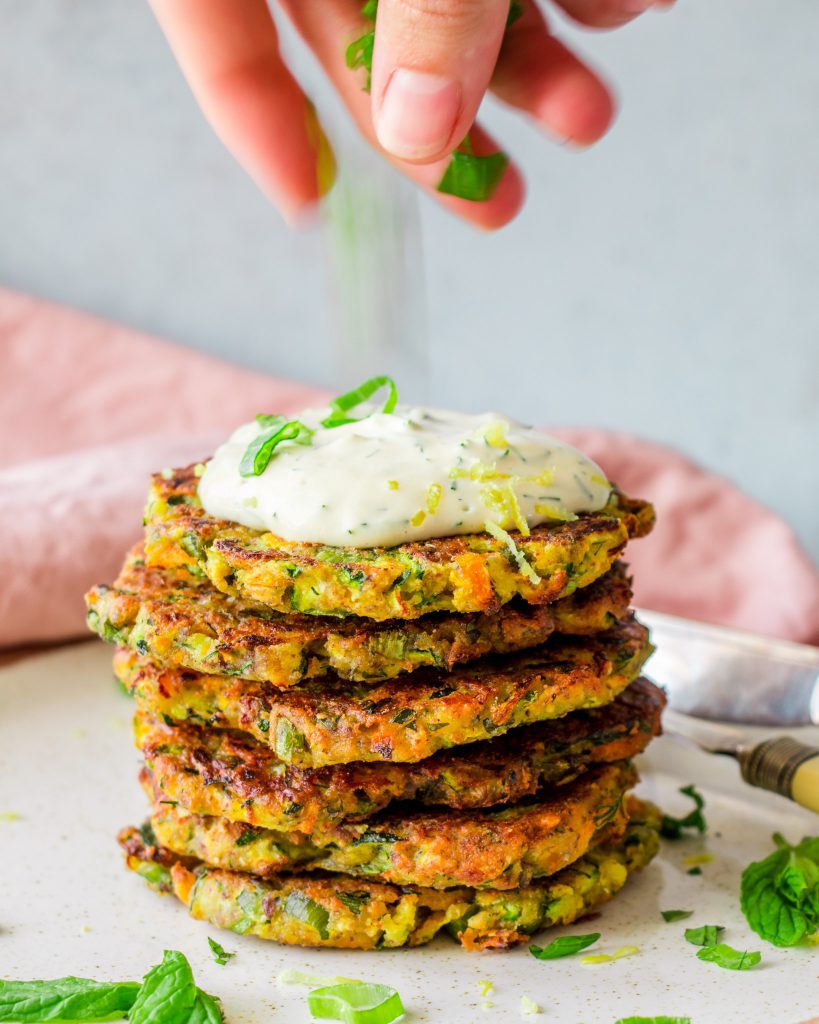 A photo of a stack of zucchini fritters with dill sauce.