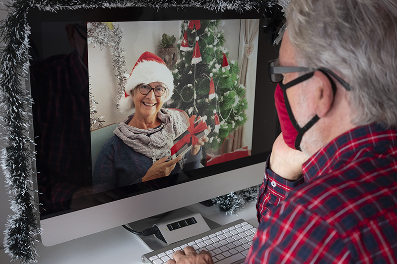 A photo of an older man video chatting with a woman in a Santa hat.
