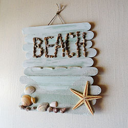 A sign made of popsicle sticks, featuring the word Beach and decorated with shells.