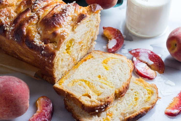 A photo of a cut loaf of peach bread surrounded by peaches and peach slices