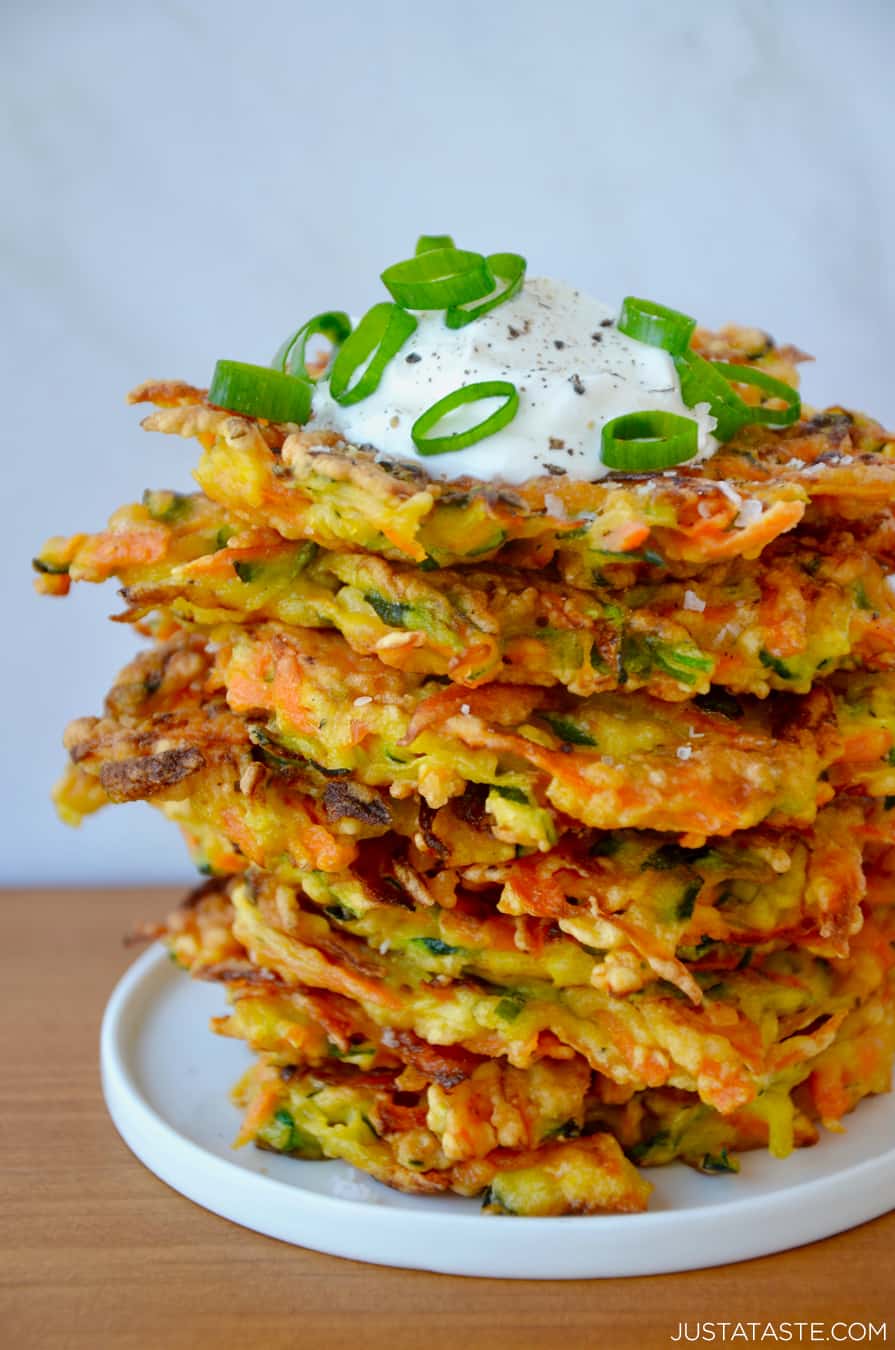 A color photo of a stack of vegetable fritters topped with a dollop of sour cream.
