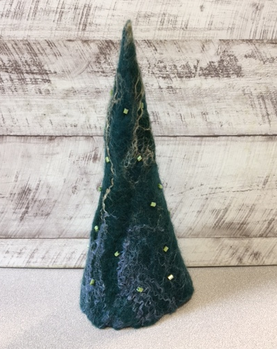 Photo of a Nuno felted holiday tree in front of a light wood background.