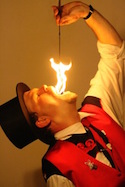 A color photo of magician Bob McEntee, dressed in a red vest and black top hat, performing a fire-swallowing stunt.