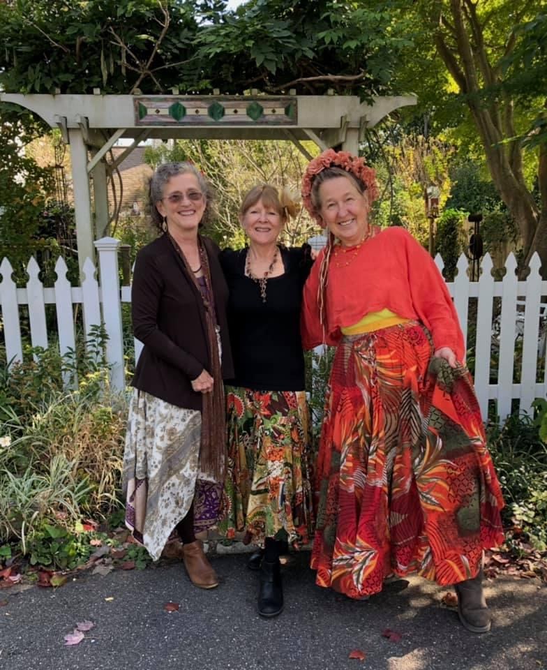 A color photo of the three members of the Mountain Maidens standing together in front of a white picket fence.