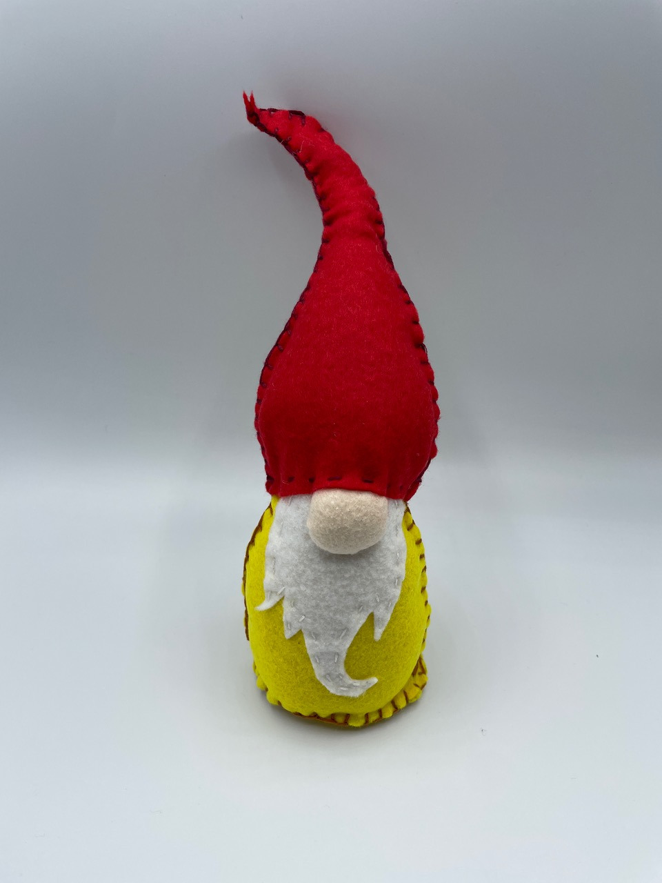 A color photo of a gnome made from felt with a red hat and yellow body.