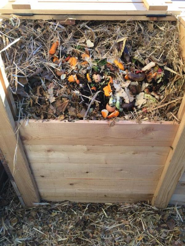 A color photo of a wooden compost bin containing material such as yard waste and food scraps.