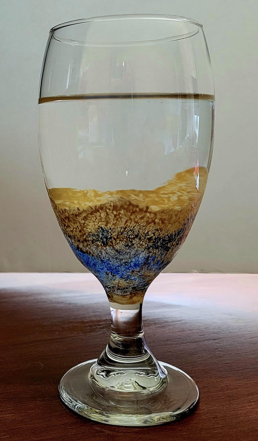 A glass goblet decorated with paint and filled two-thirds with water.