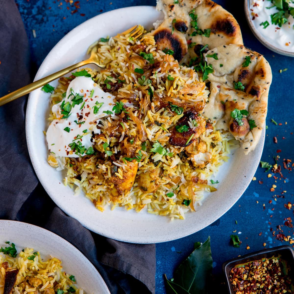 A color photo of a white bowl filled with chicken biryani and rice.