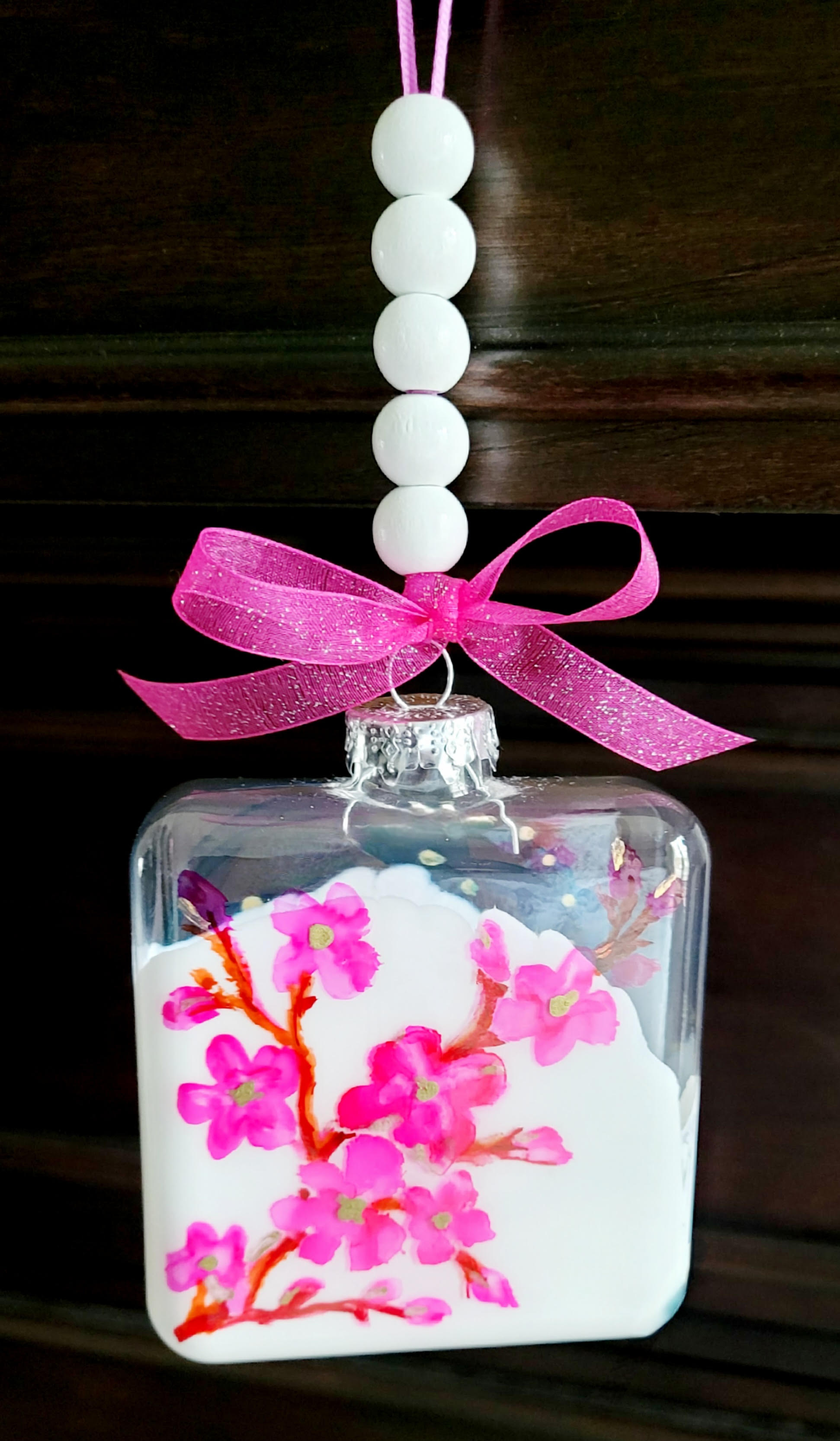 A color photo of a decorative ornament featuring a beaded hanger and pink bow.
