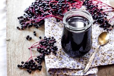 A photo featuring a jar of elderberry syrup, elderberries and a spoon.