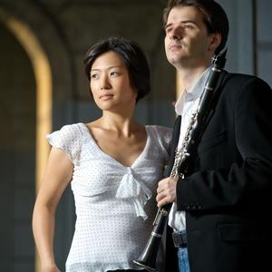 A color photo of pianist Misuzu Tanaka in w white dress and clarinetist Maksim Shtrykov in a black suit jacket, holding a clarinet.