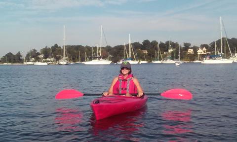 Photo of a woman sitting in a red kayak on the water in Huntington Harbor.