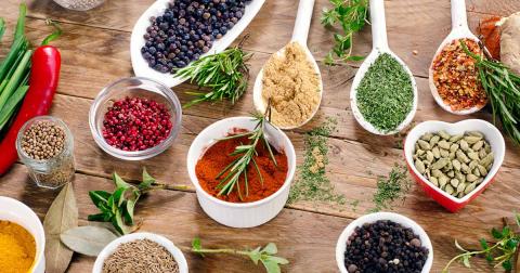 A photo of white bowls and spoons holding assorted herbs and spices.