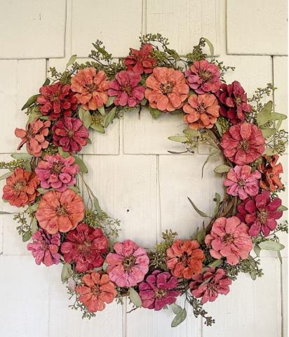 A color photo of a wreath created mostly from pinecones painted to look like flowers.
