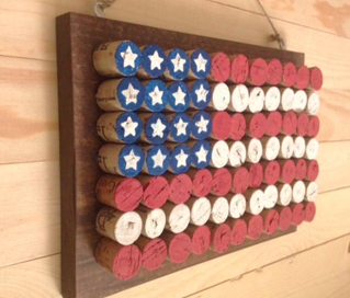 A color photo of an American flag made from wine corks painted red, white and blue hanging on a wood-paneled wall.