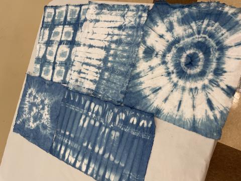 A color photo of four squares of white fabric dyed blue using the Shibori technique.