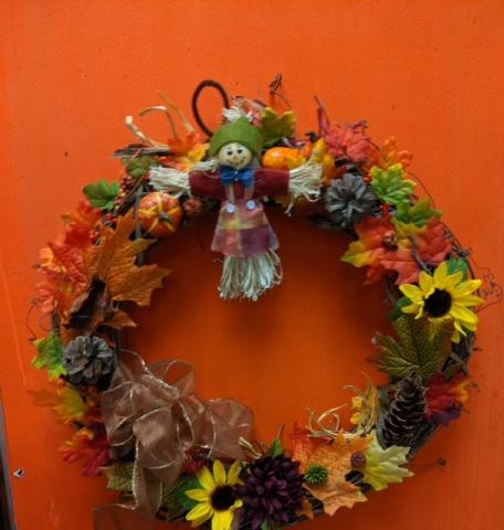 A color photo of an autumn wreath adorned with flowers and leaves.