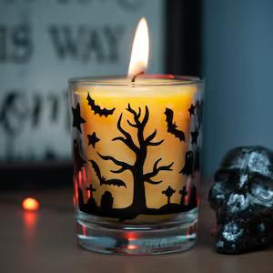 A glass candle holder adorned with black bats and the silhouette of a tree.