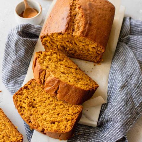 A photo of a loaf of pumpkin bread on a cutting board with two slices cut from it.