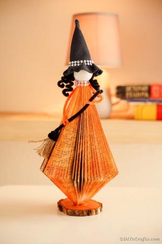 A color photo of a witch doll whose orange skirt is made from folded book pages.