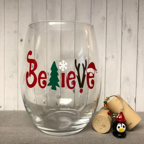 A stemless wine glass with the word Believe on it in red and green.