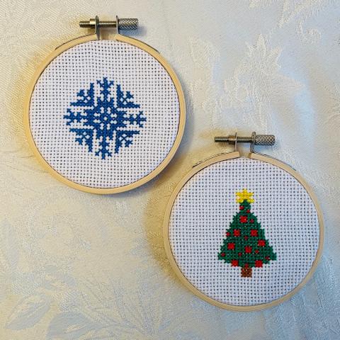 A photo of two cross stitch designs, a blue snowflake and a green pine tree.