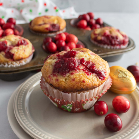 A photo of a cranberry eggnog muffin on a plate with a few cranberries alongside.