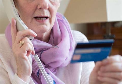 A photo of a woman on the phone holding a credit card.