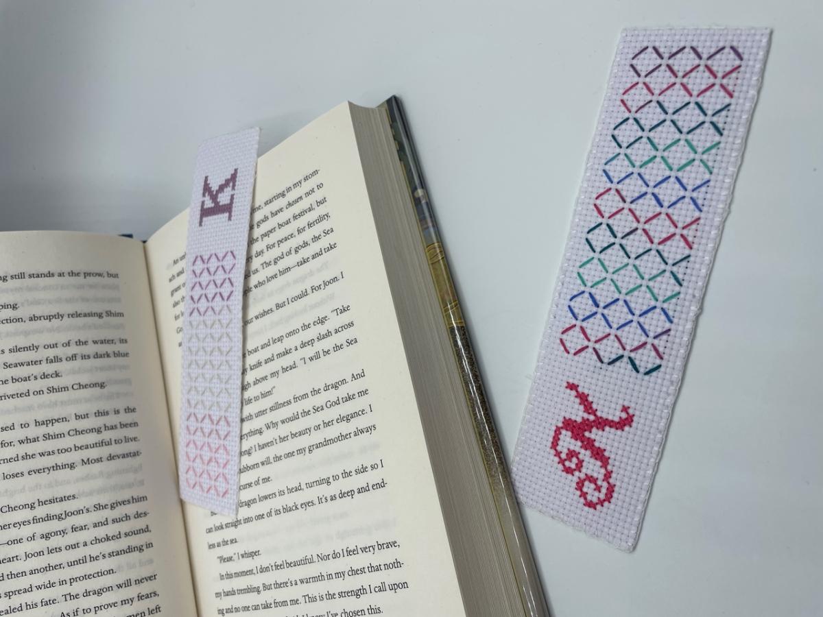 A color photo of an open book accompanied by two bookmarks decorated with cross stitches and initials.