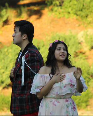 A color photo of one male and on female actor in period costume performing outside.