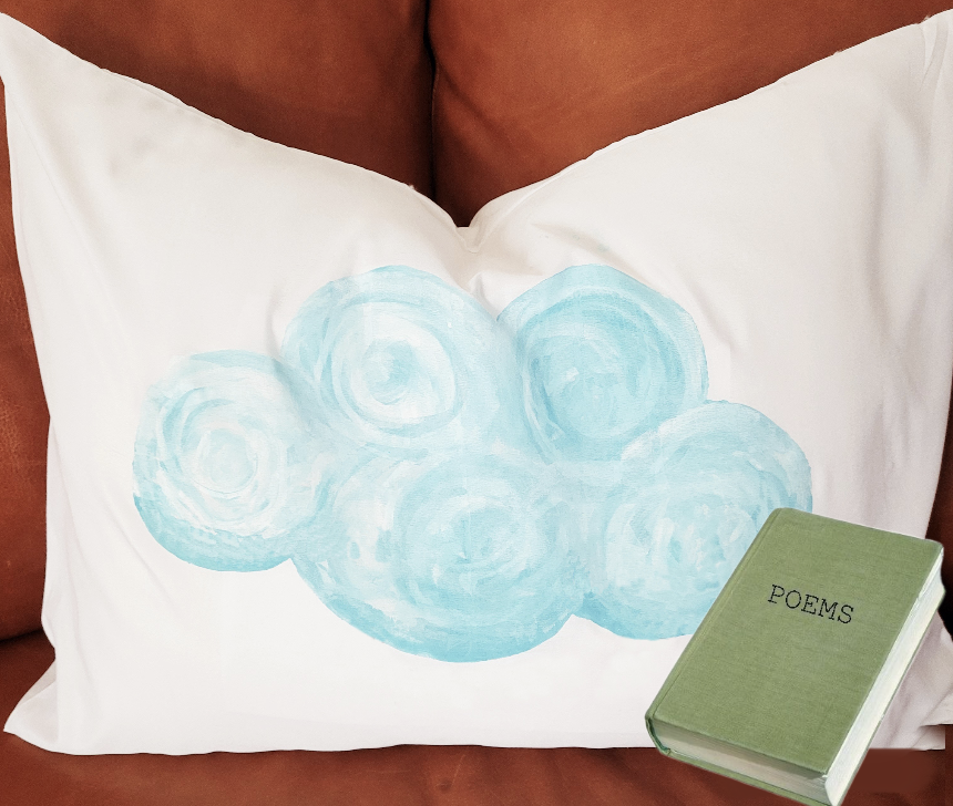 A color photo of a white pillow cover that has been painted with light blue clouds.