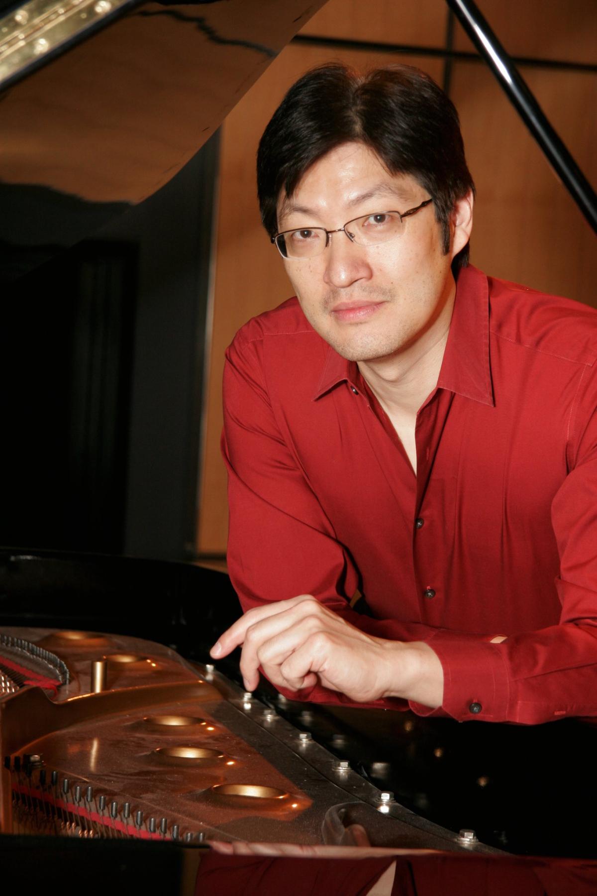 A color photo of pianist Alex Wu in a red shirt and leaning on a piano.