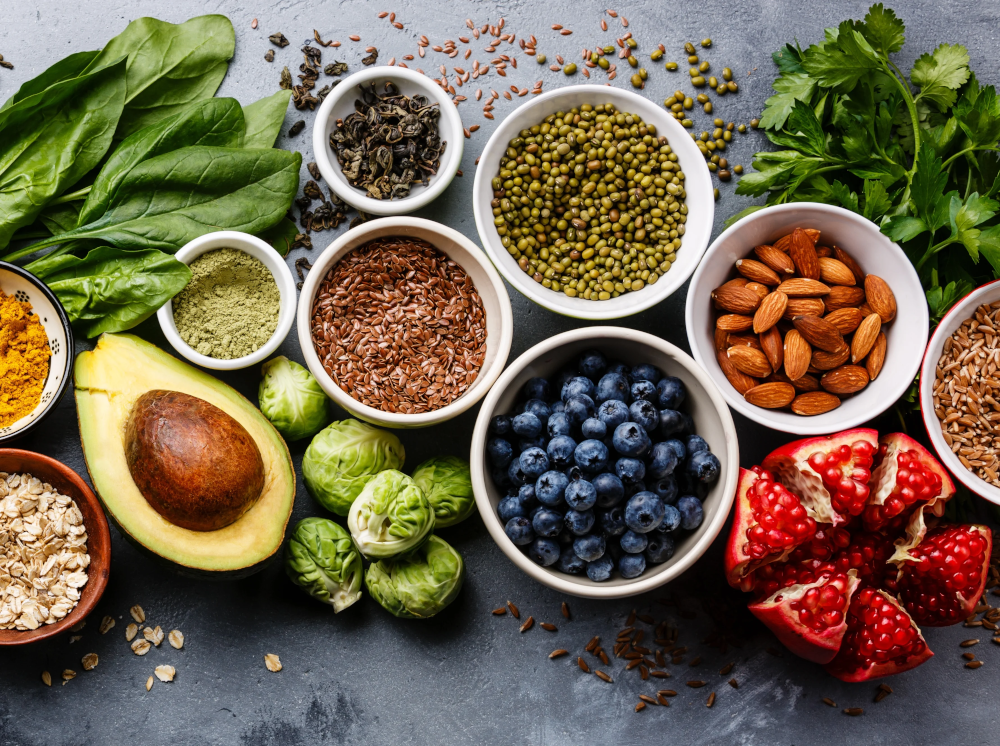 A color photo of a variety of superfoods, including blueberries, almonds, avocado, greens, beans and seeds.