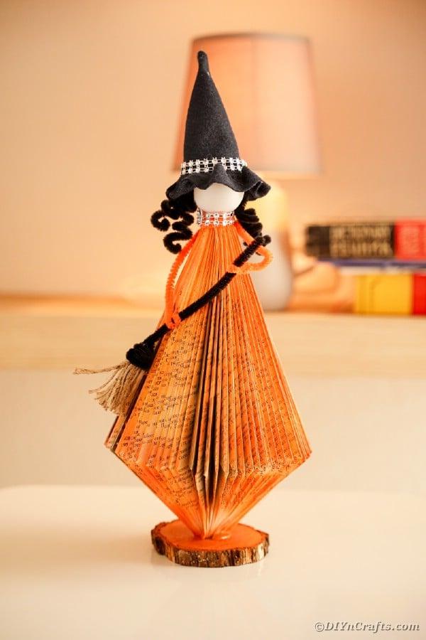A color photo of a witch doll whose orange skirt is made from folded book pages.