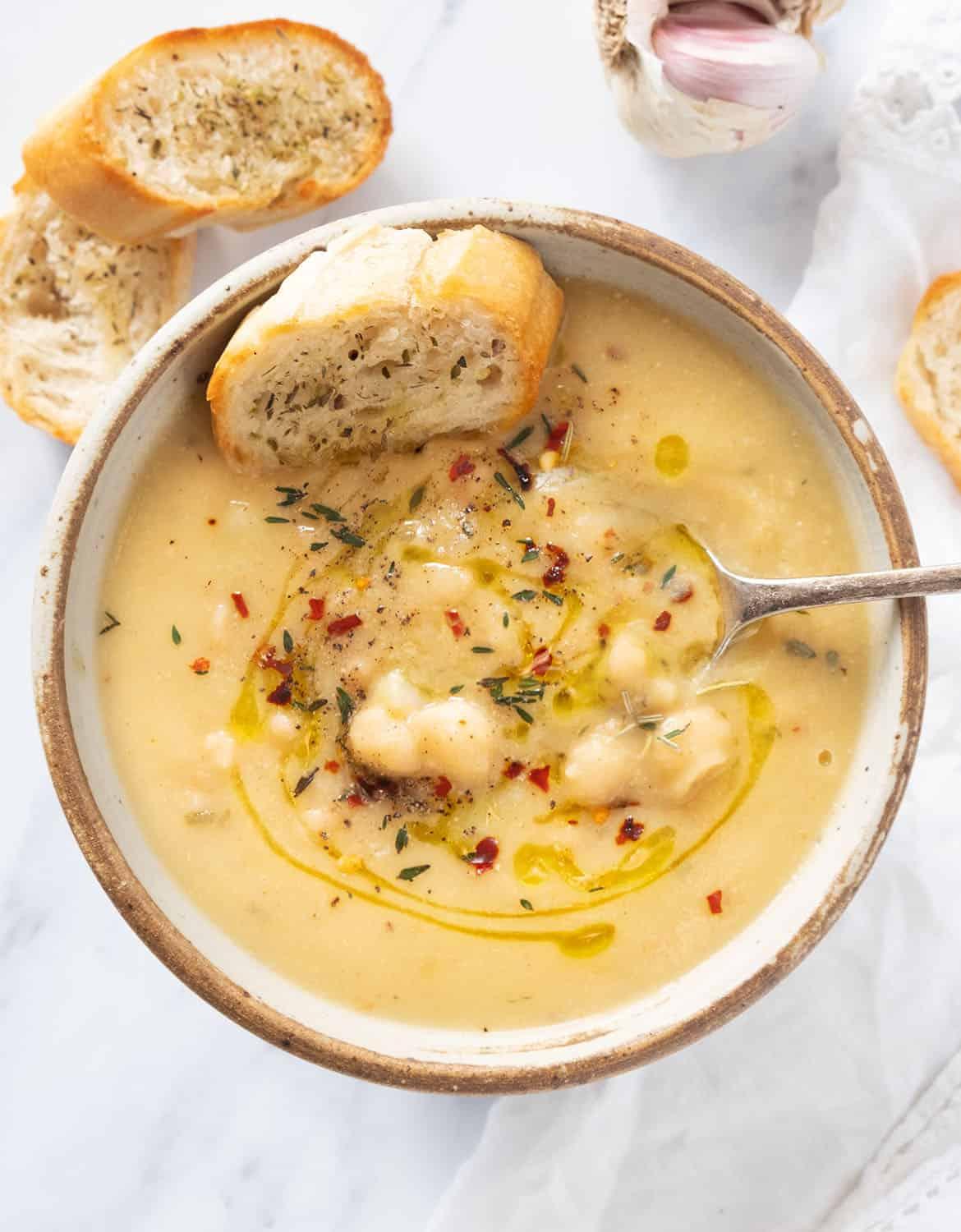 A photo of a bowl of chickpea soup with a spoon in it and bread on the side.