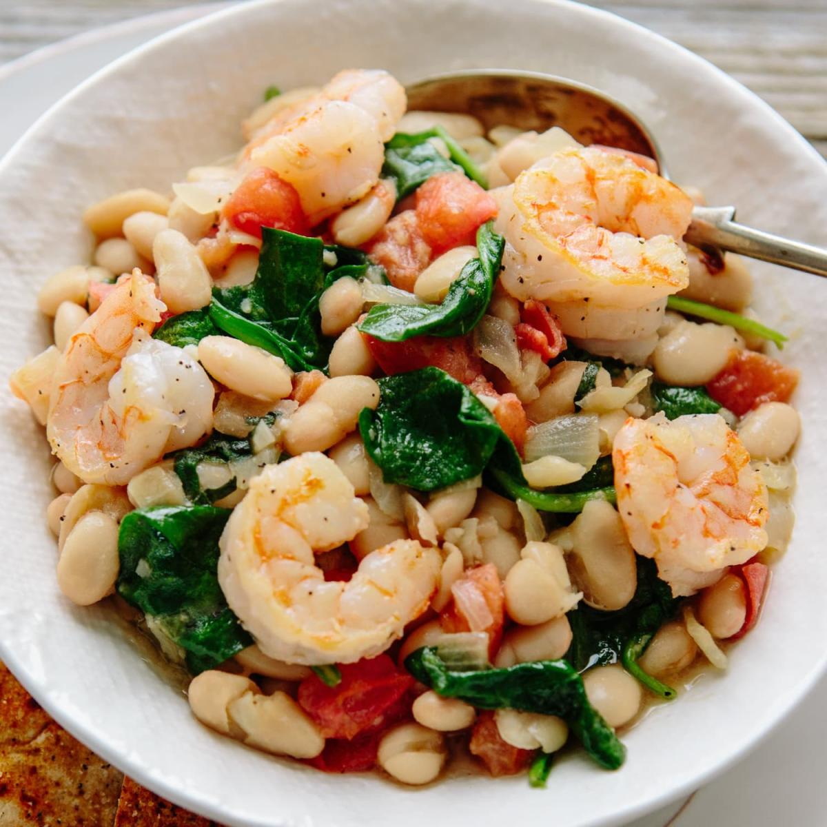 Photo of a white bowl filled with shrimp and white beans.